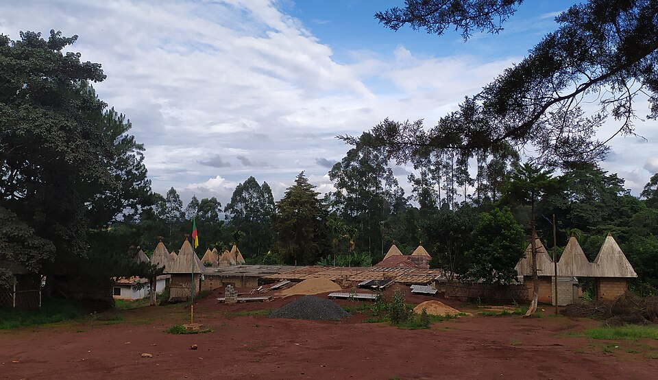 Vue de la chefferie de Batcham avec bâtiments à toitures coniques parmi les arbres